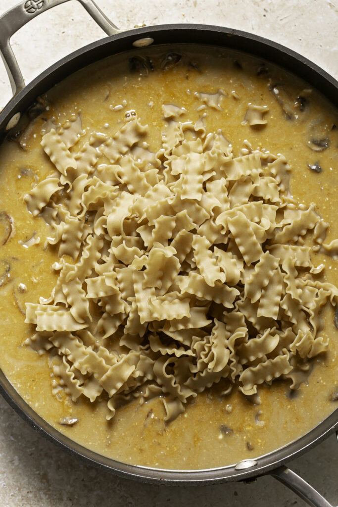 dry pasta noodles added to a skillet with broth in it.