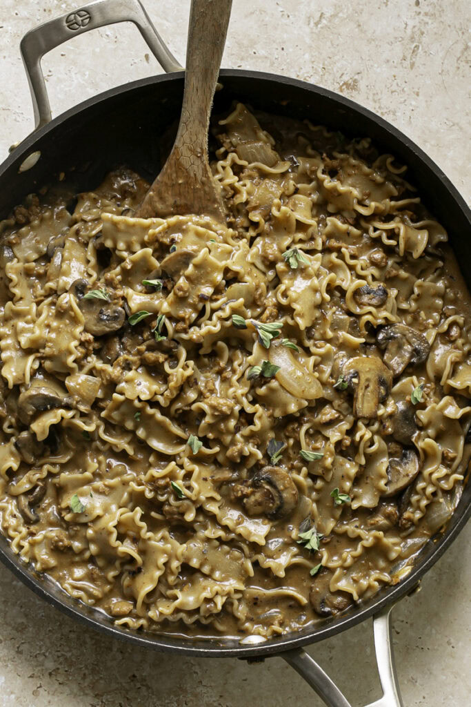 cooked homemade one pan vegan beef stroganoff hamburger helper in a skillet with a wooden spoon.