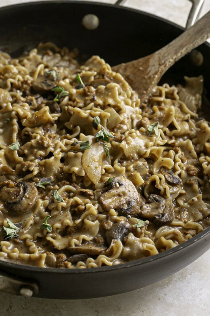 cooked homemade one pan vegan beef stroganoff hamburger helper in a skillet with a wooden spoon.