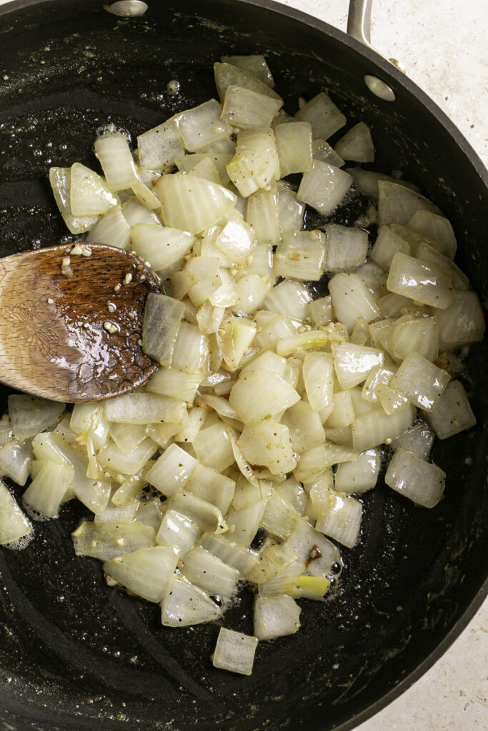 sauteed onions in a skillet with a wooden spoon.