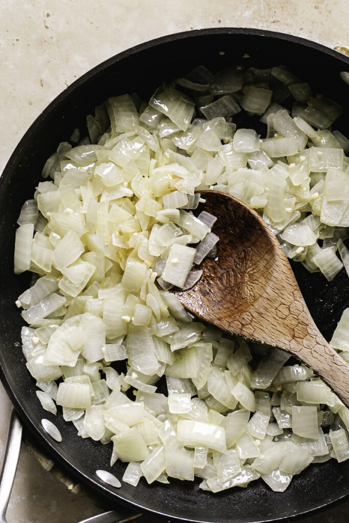 sauteed onions in a skillet with a wooden spoon.