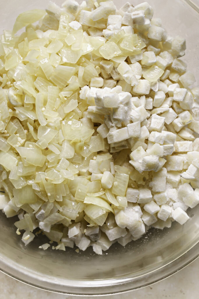 sauteed onions in a bowl with frozen diced hashbrown potatoes.