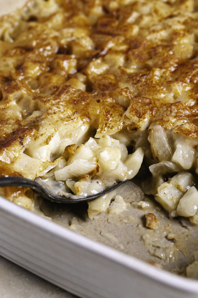 3/4 shot of creamy vegan hashbrown casserole in a baking dish with a serving spoon in the casserole dish.