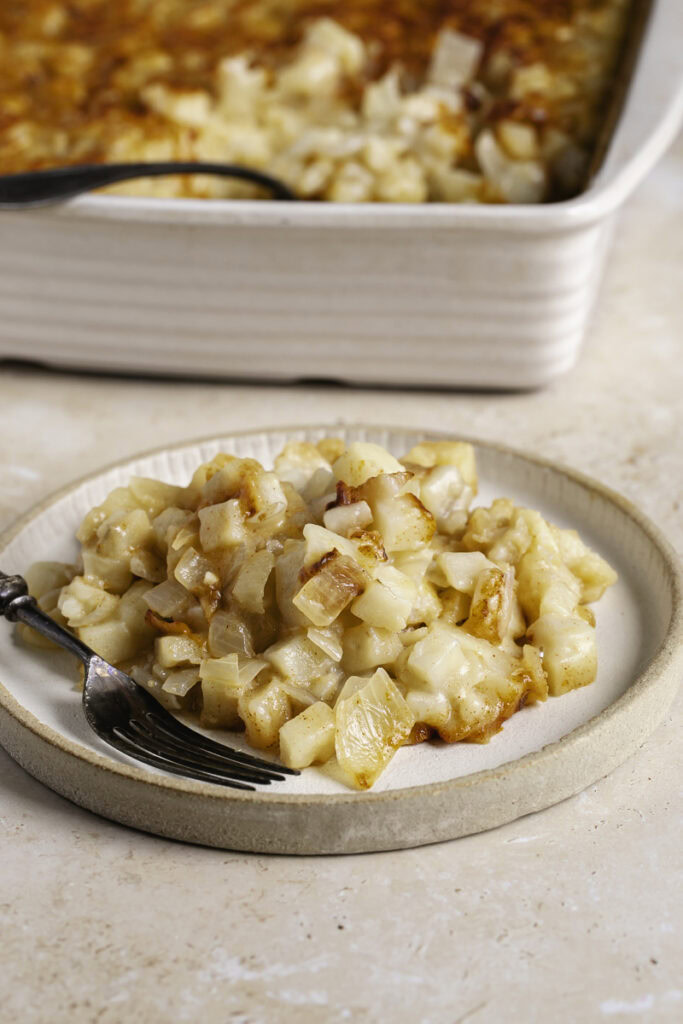 hashbrown casserole served on a plate with the casserole dish in the background.