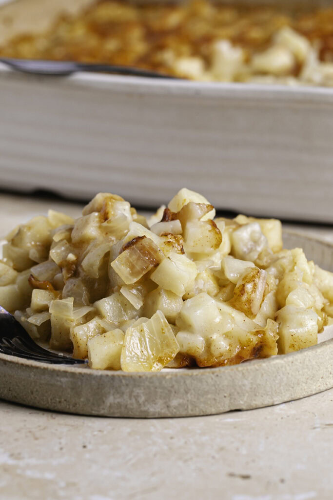 close up of hashbrown casserole served on a plate with the casserole dish in the background.