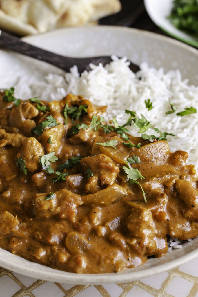 close up of indian butter chicken over rice in a bowl with a spoon.