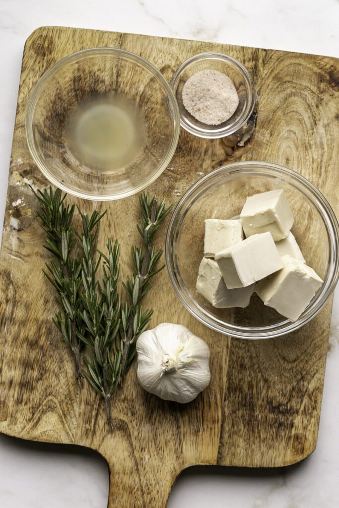 Fresh rosemary, lemon juice, salt, butter, garlic on a wooden cutting board.
