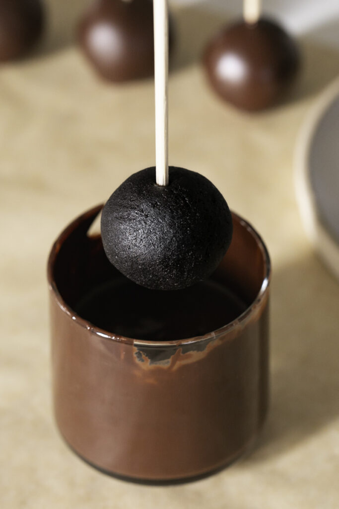 action shot of a brownie bite on a stick held over a glass of melted chocolate.