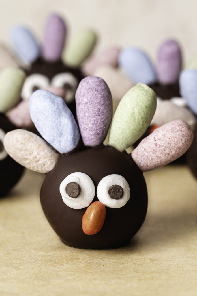 a close up of a no-bake date almond flour brownie bite turkey with pastel colored almond feathers, googly eyes and a candy beak.