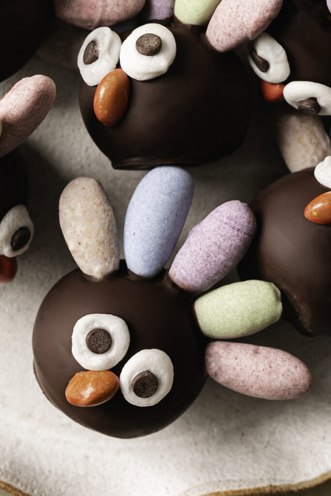 close up overhead shot of no-bake date almond flour brownie bite turkeys with pastel colored almond feathers, googly eyes and a candy beak.