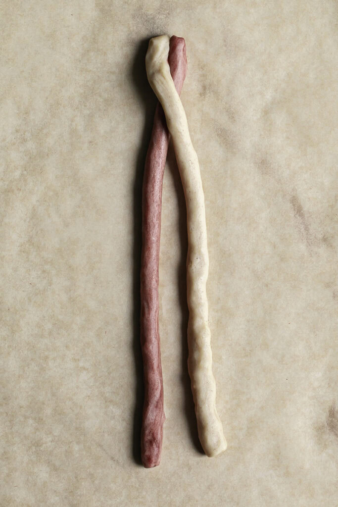 two rolled out pieces of cookie dough, one red and one white crossed over each other at the top.