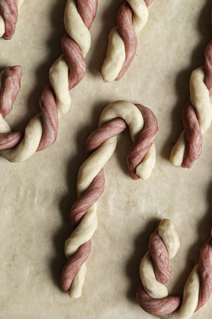 unbaked cookie dough candy canes on parchment paper.