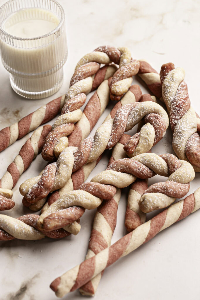shortbread candy cane cookies piled on top of each other next to a glass of oat milk.