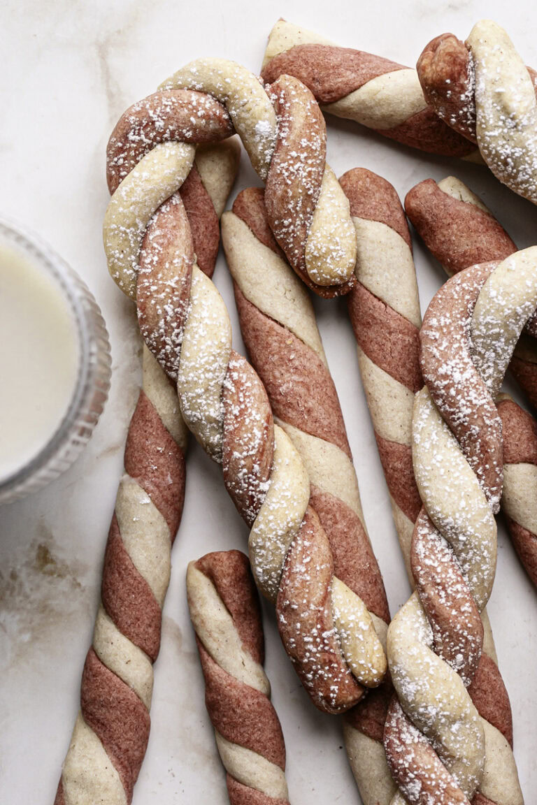shortbread candy cane cookies piled on top of each other next to a glass of oat milk.