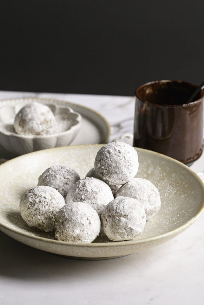 powdered sugar donut holes in a plate with a glass of melted chocolate and a small bowl of powdered sugar with a donut hole in it.