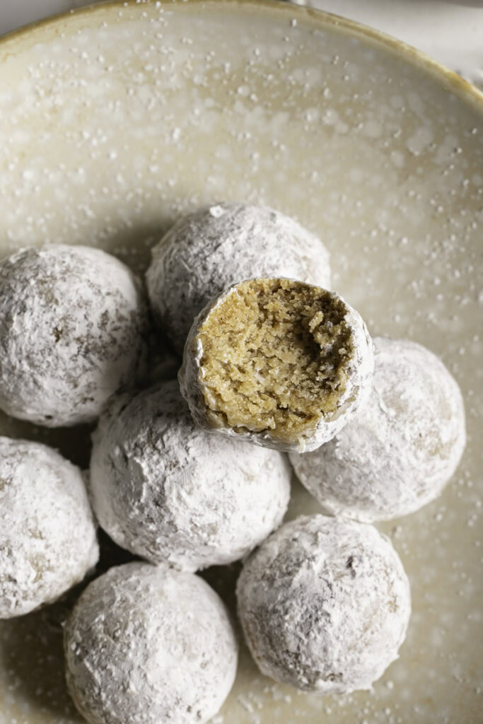 overhead shot of powdered sugar donut holes in a plate, one with a bite taken out of it.