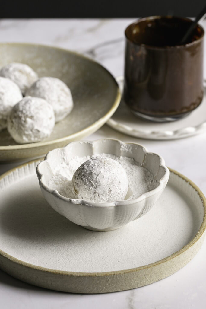 a donut hole in a small bowl of powdered sugar with others in a bowl behind it.