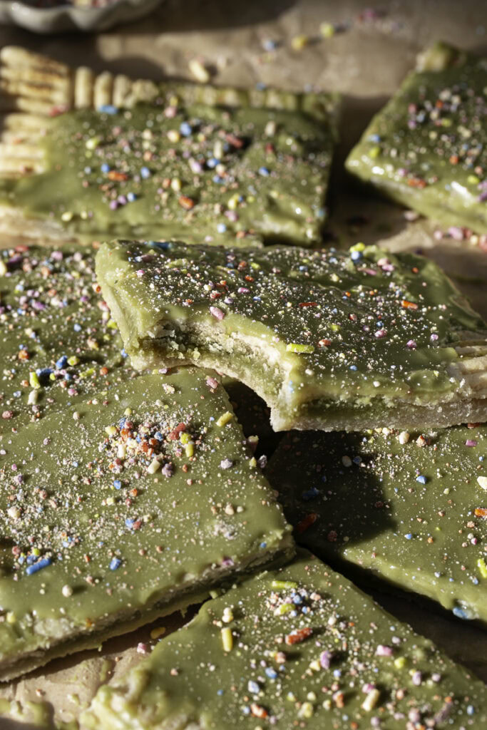 slices of giant frosted matcha pop tart stacked on top of one another, the top one with a bite taken out of it.