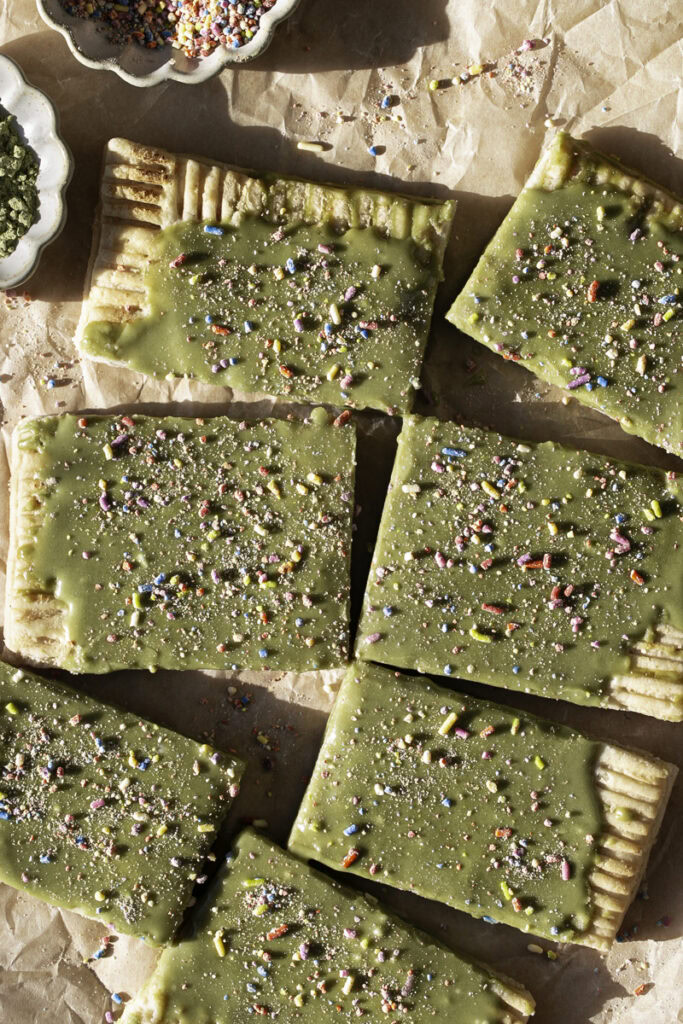 cut slices of a giant frosted matcha pop tart decorated with sprinkles.