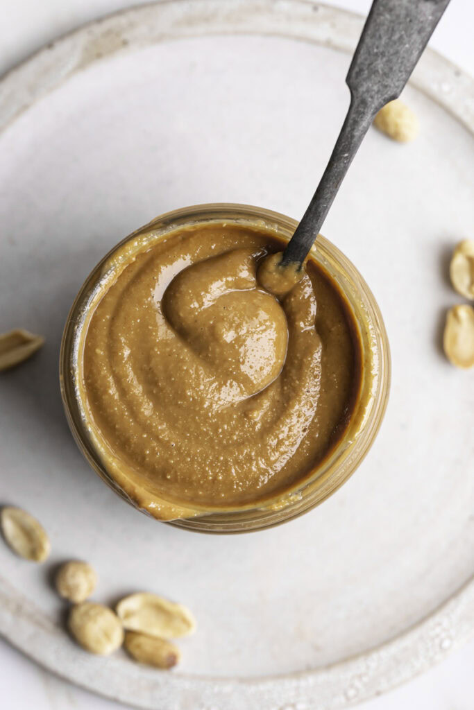 an overhead shot of a jar of homemade roasted peanut butter with a spoon sticking out of it.