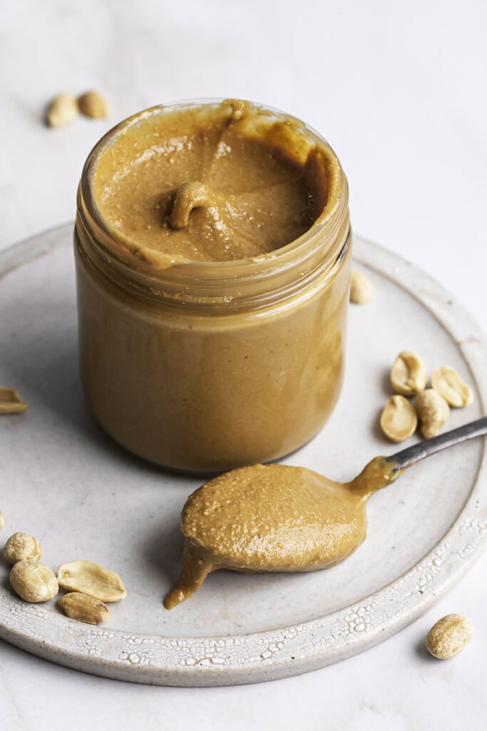 a jar of peanut butter with a spoonful of peanut butter resting on a plate in front of the jar.