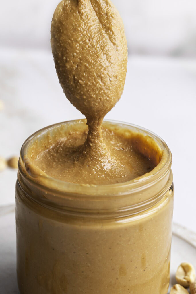 a spoonful of peanut butter drizzling off the spoon into the jar of peanut butter.
