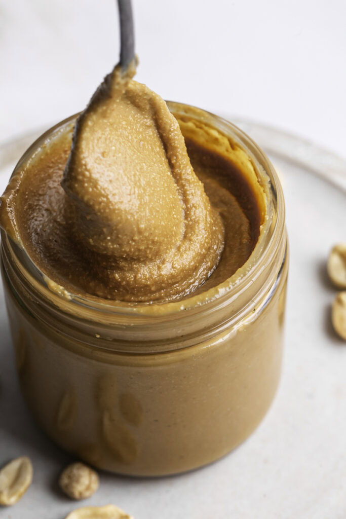 close up of a jar of homemade roasted peanut butter with a spoon swirling around in it.