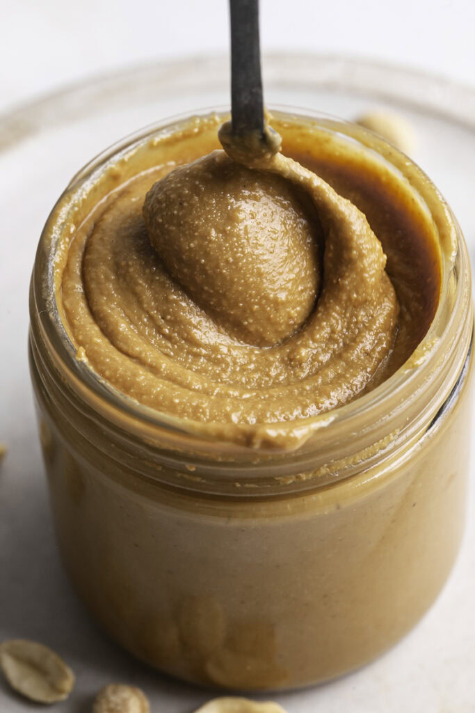 close up of a jar of homemade roasted peanut butter with a spoon swirling around in it.
