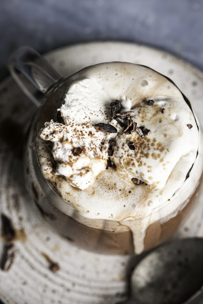 overhead shot of hot cocoa in a glass mug topped with whipped cream.