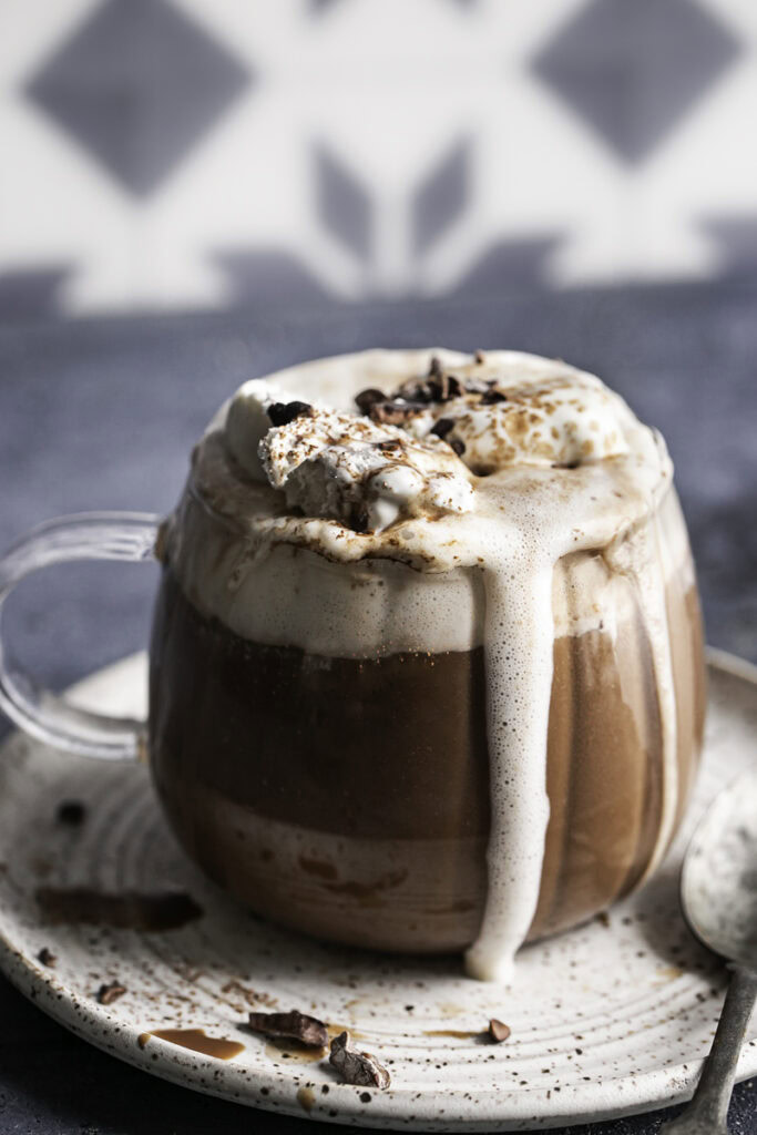a close up of glass of oat milk hot cocoa overflowing with whipped cream.