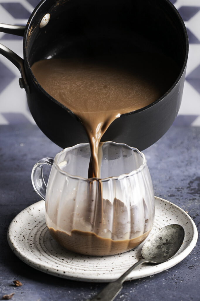 action shot pouring hot cocoa in a glass mug from a saucepan.