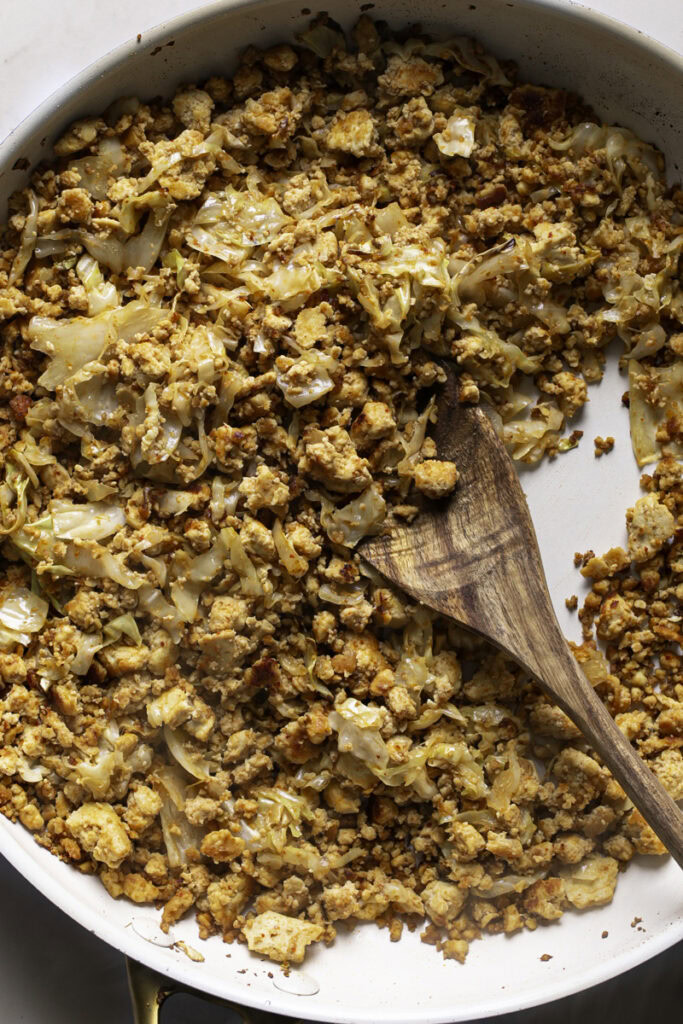 sauteed tofu and cabbage in a skillet with a wooden spoon.