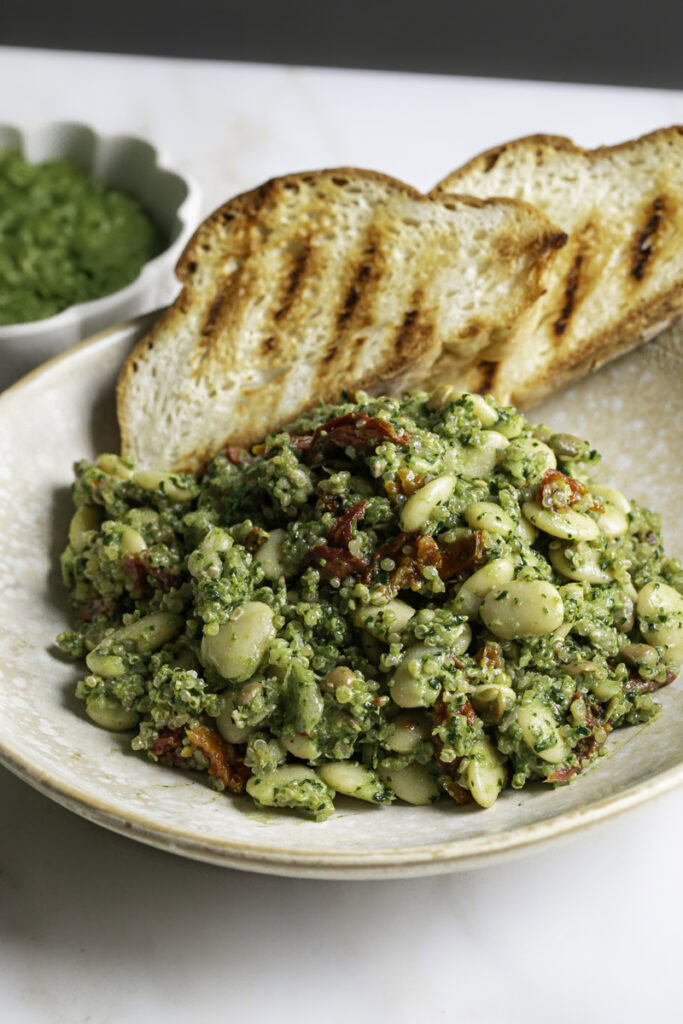 3/4 shot of a close up of spinach pesto butter bean lentil quinoa with two slices of grilled bread.
