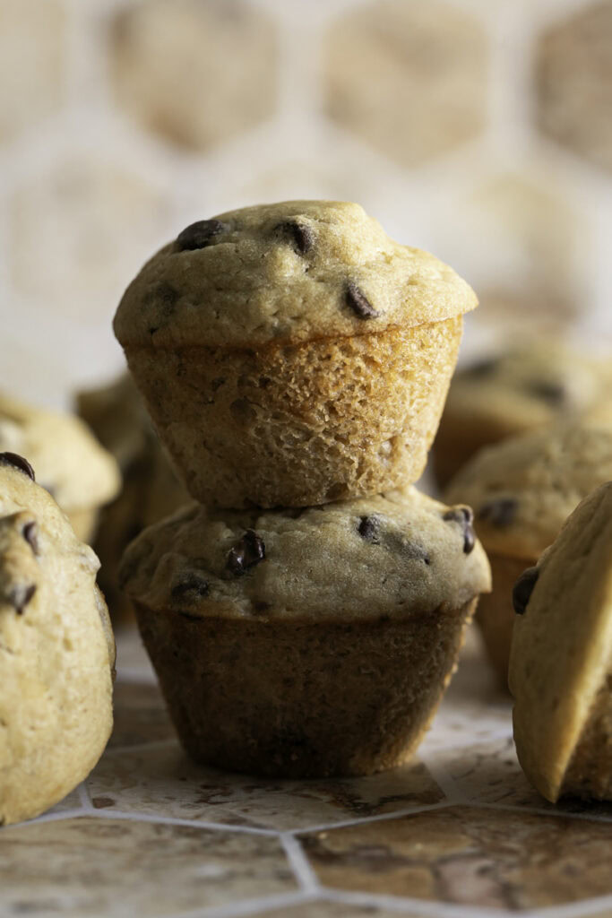 A close up of two mini buckwheat flour chocolate chip banana muffins stacked on top of one another.