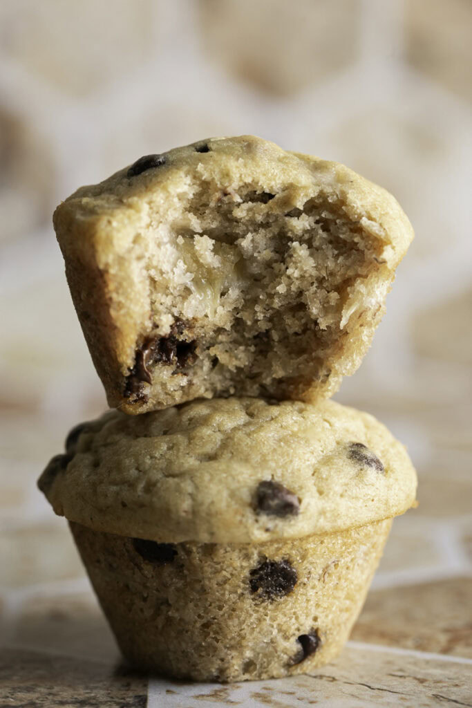 two mini buckwheat flour chocolate chip banana muffins stacked on top of one another, the top one with a bite taken out of it.