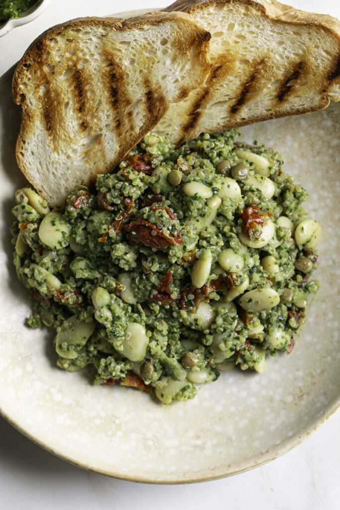 overhead shot of a close up of spinach pesto butter bean lentil quinoa with grilled bread.