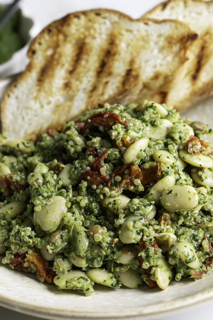 extreme close up shot  of spinach pesto butter bean lentil quinoa with two slices of grilled bread.