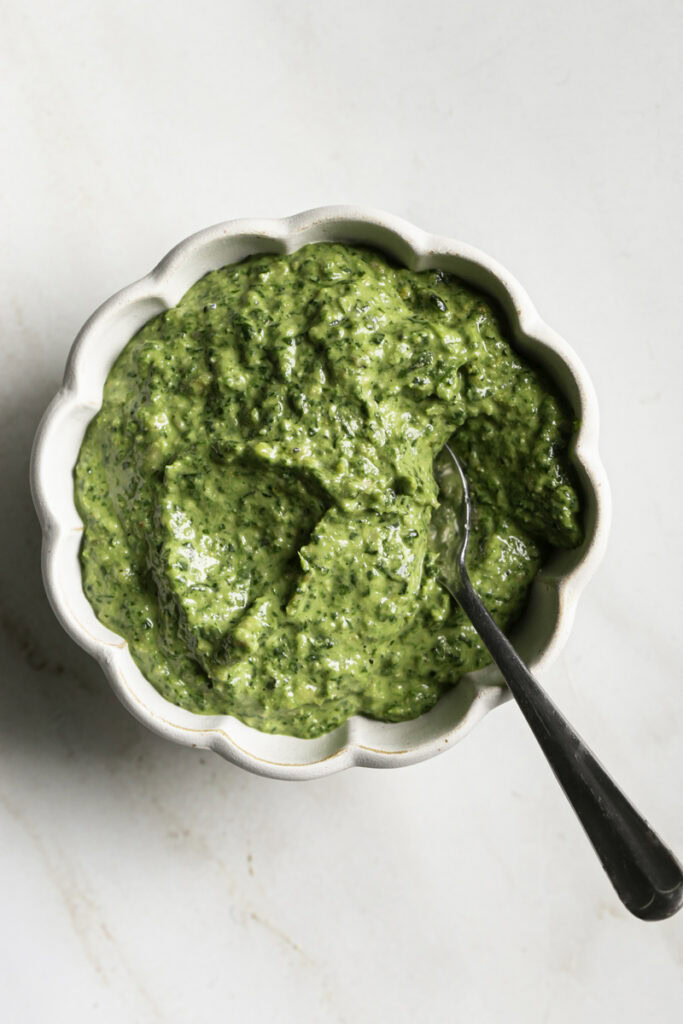 a bowl of spinach pesto with a spoon in it.