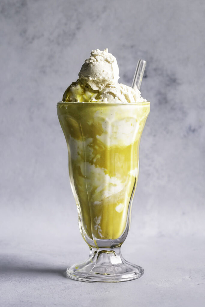 golden milk ice cream float in a tall glass with a glass straw.