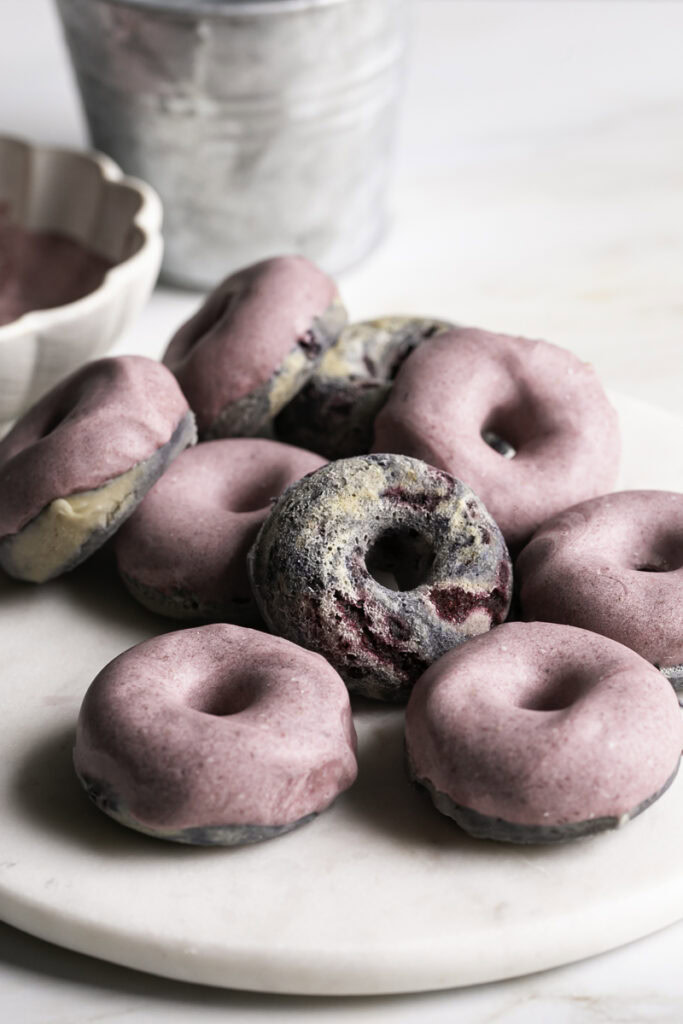 mini baked black berry cake donuts with blackberry frosting on a marble plate with
