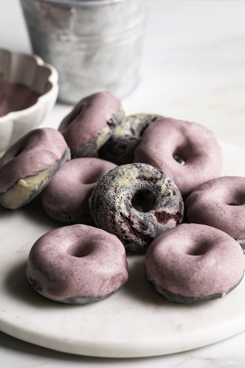 mini baked black berry cake donuts with blackberry frosting on a marble plate with