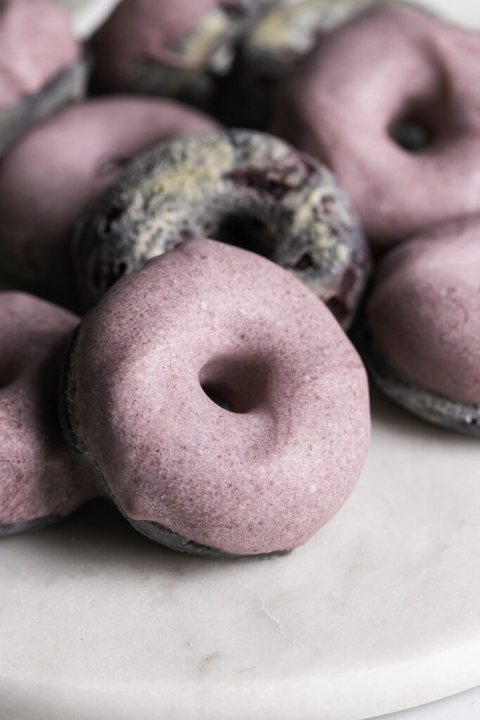 close up of a mini baked blackberry cake donut dipped in blackberry white chocolate.