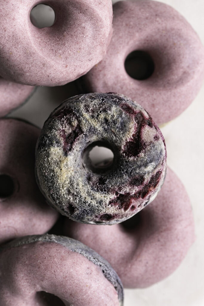overhead shot of mini baked blackberry donuts, the center one not dipped in blackberry white chocolate.