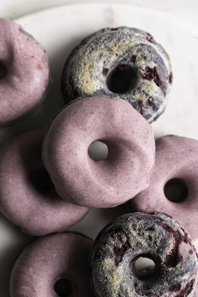 overhead shot of mini baked blackberry cake donuts piled on top of one another.