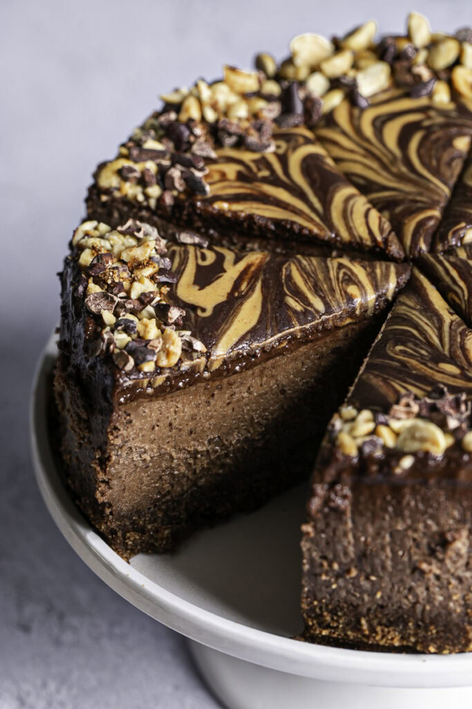 sliced vegan triple chocolate peanut butter cheesecake on a cake stand.