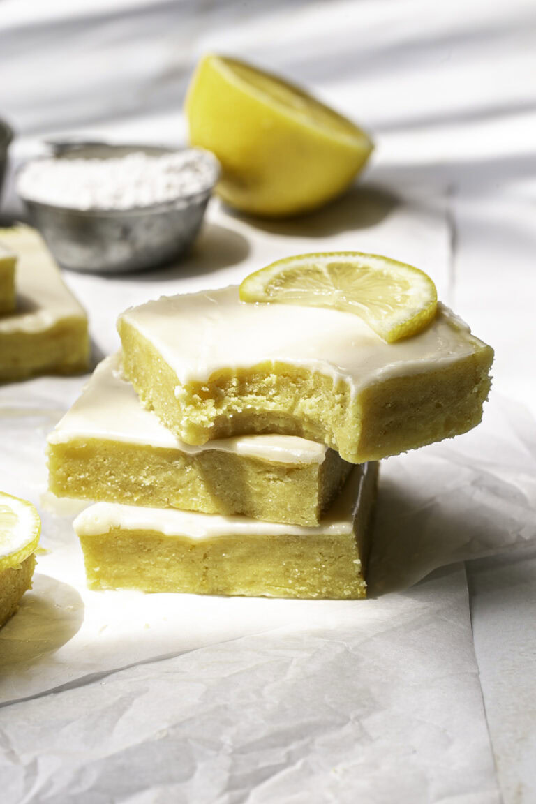 three No-Bake Almond Flour Lemon Brownies stacked on top of one another, the top slice with a bite taken out of it.