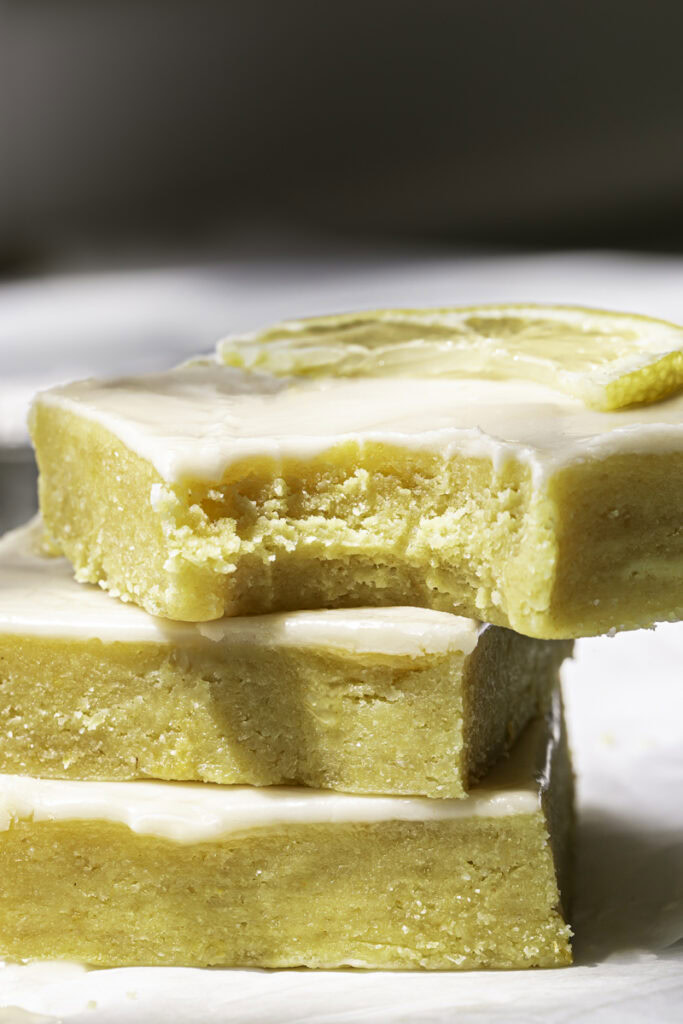 close up shot of three No-Bake Almond Flour Lemon Brownies stacked on top of one another, the top slice with a bite taken out of it.