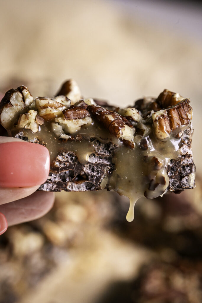 a hand holding a turtle crispy rice square with caramel dripping off.