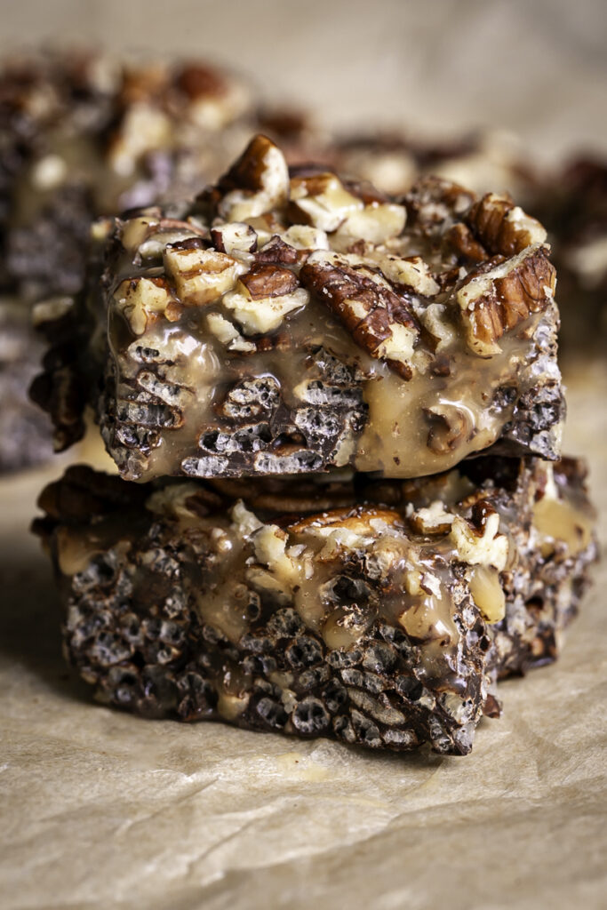 close up of two turtle crispy rice squares stacked on top of one another on a piece of parchment paper.
