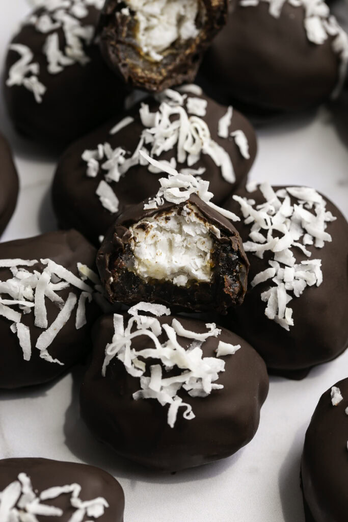 Vegan Bounty Bar Coconut Stuffed Dates in a pile, one with a bite taken out of it to reveal the coconut filling.